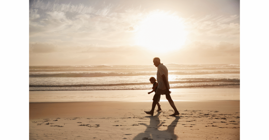 Grandfather walking with his grandchild along the beach at sunset, symbolizing presence, legacy, and the moments that matter beyond work